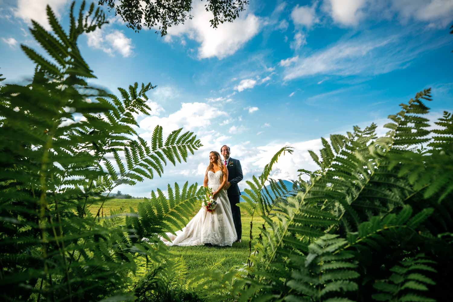 bride and groom stand amongst ferns at their wedding