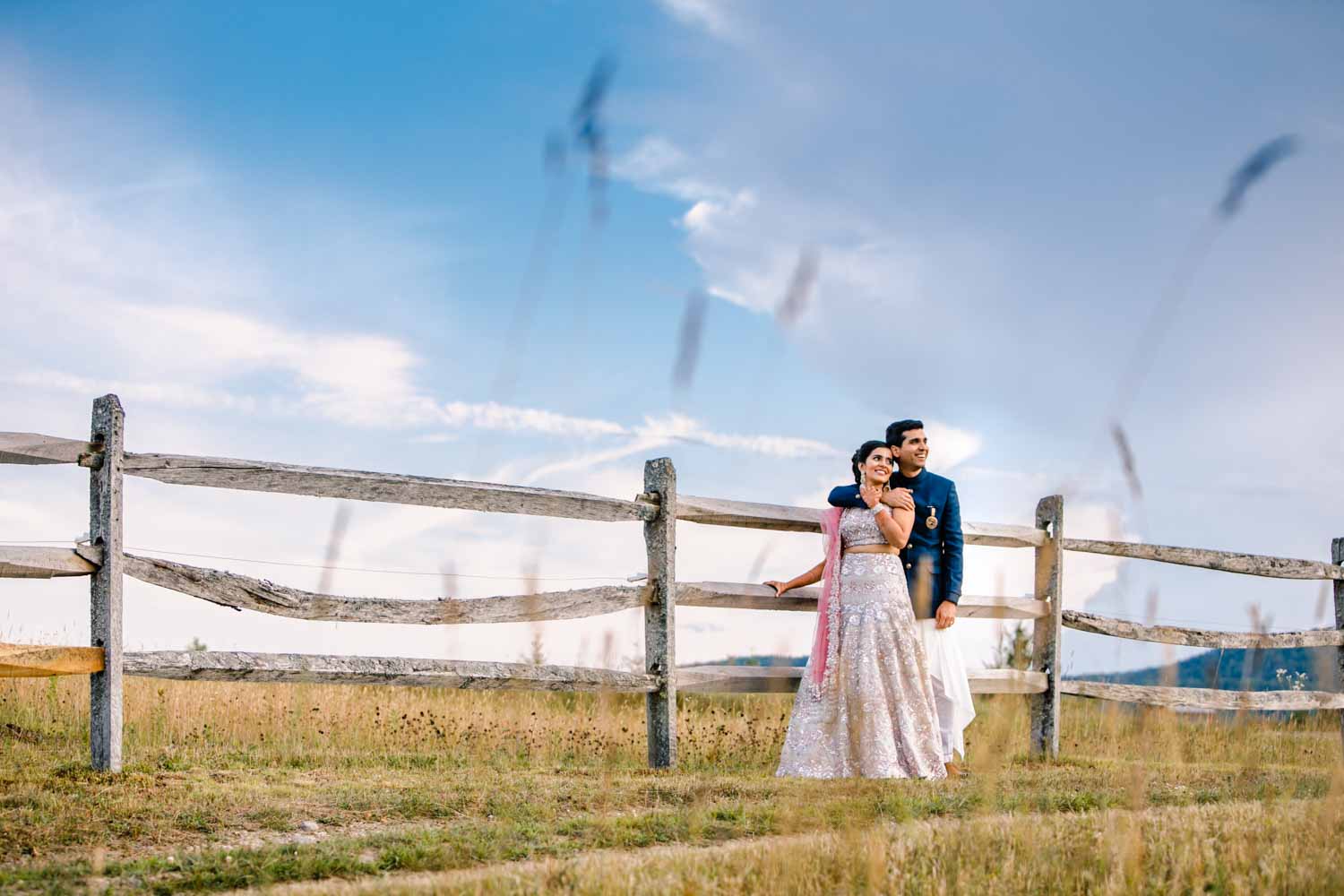 indian bride and groom lean against a fence in a field in stowe vermont